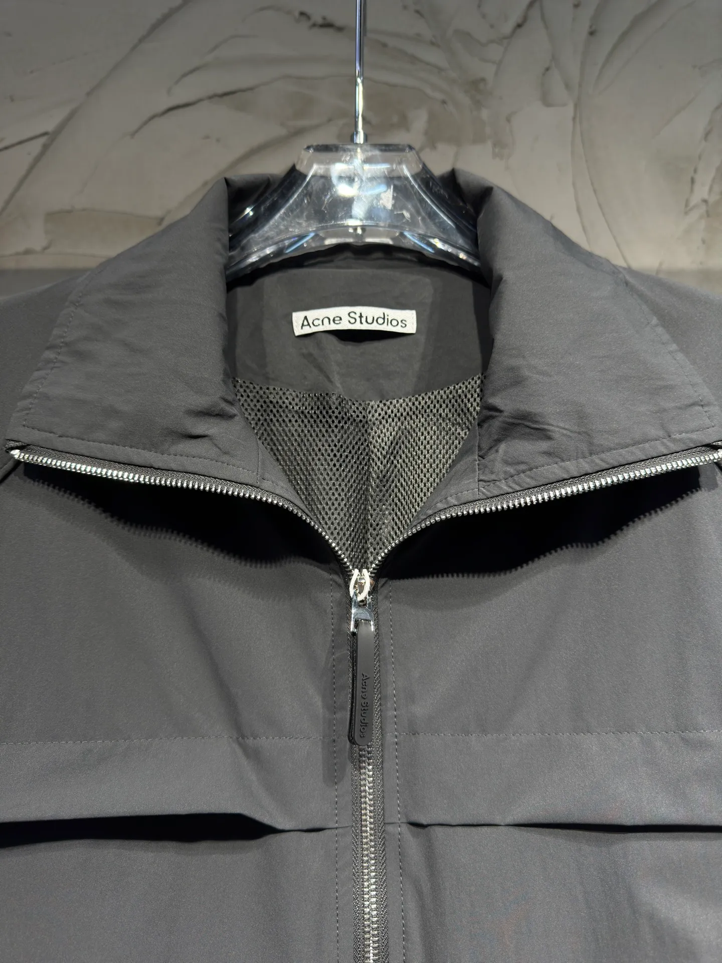 Acne Studios 26SS Large Lapel Short Jacket The fabric is made of 100% nylon (nylon/polyamide fiber) 75D high-density wrinkled nylon. The fabric has been permanently pressed and shaped by high temperature, and washed with high-pressure wrinkles at the factory to form its own irregular texture, permanently retaining the wrinkled texture, which will not disappear after washing. Matte matte coating removes the plastic glossy surface of nylon itself to create a low-key matte paper feel. Three-proof micro-coating, weak waterproof, anti-fouling, anti-static treatment, not easy to get dust. The interior is made of full-width mesh Breathable nylon lining, which reduces the stickiness of the nylon fabric to the body, improves air circulation, prevents sweating from sticking to the skin, and the zipper does not rub against the skin. The version adopts the raglan split topstitching process, and the front and rear panels are divided diagonally to expose even stitching. The three-dimensional dropped shoulders are loose and the fit is increased to increase the margin of movement. The back neckline is three-dimensional and high-density computer embroidered, and the embroidery lines are dense and not prickly. Customized all-metal matte nylon zipper, Genuine Leather embossed brand letters on the zipper leather tab, zipper tape with same color nylon fit to the body, double-locked reinforcement on both sides of the zipper to prevent pulling and tearing. Color: Gray Size: S M L